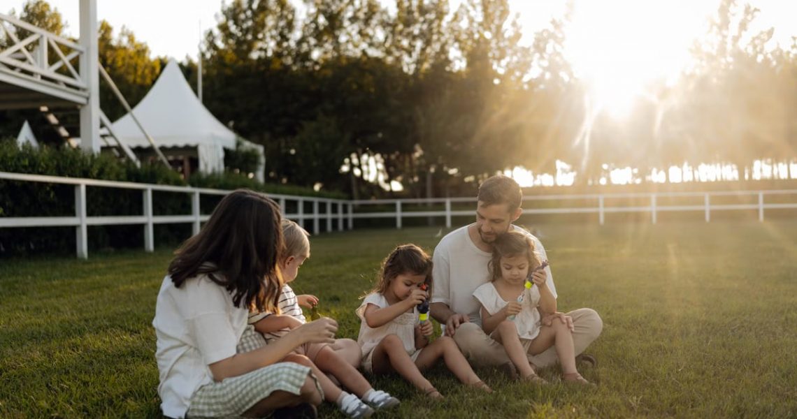 Family sitting on grass enjoying leisure time outdoors, with sun setting in the background.