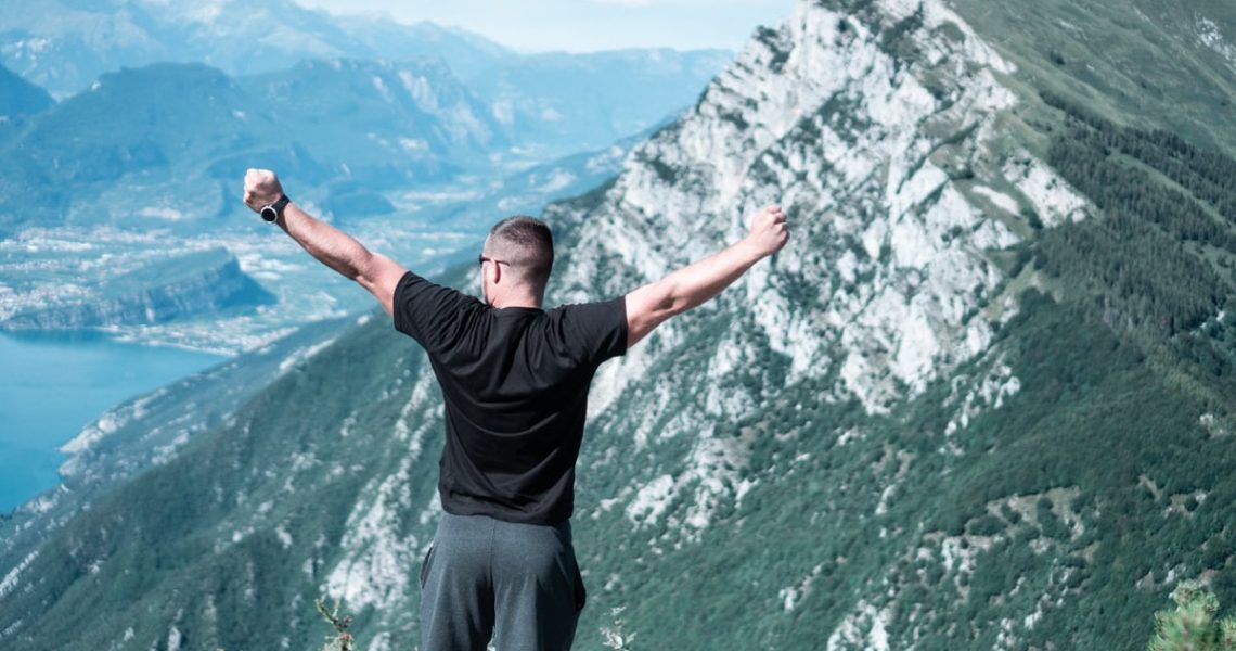 Man standing with arms raised in celebration overlooking a breathtaking mountain landscape.